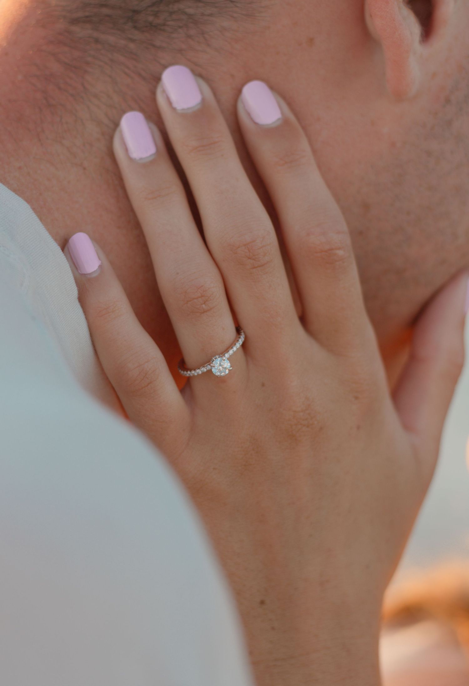 Close-up of a diamond solitaire engagement ring on a woman's hand with pink manicured nails.
