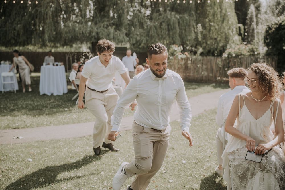 Guests dancing joyfully outdoors at a summer wedding reception in a lush green garden setting.