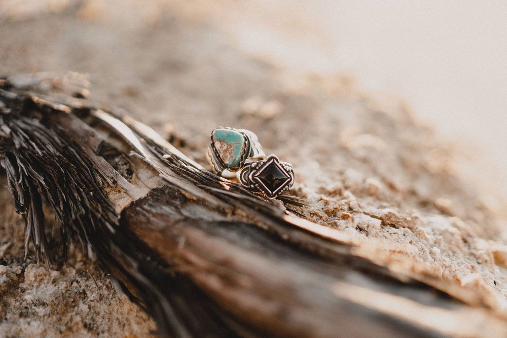 Two silver rings with turquoise and dark gemstones displayed on rustic natural wood surface in New Mexico