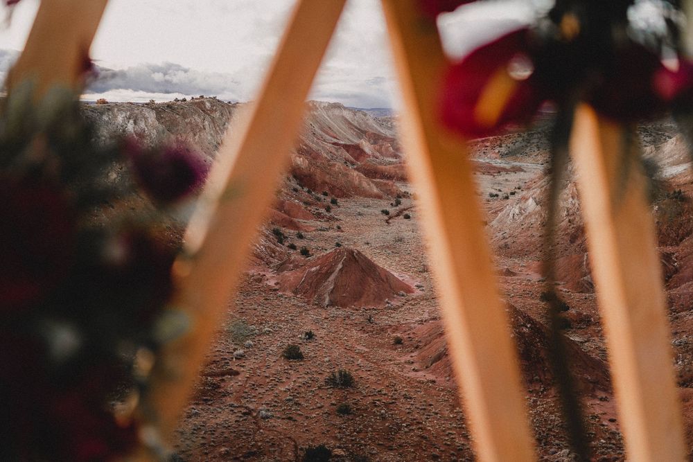 View through wooden triangular wedding arch of dramatic red and orange desert canyon landscape below in Ojito Wilderness