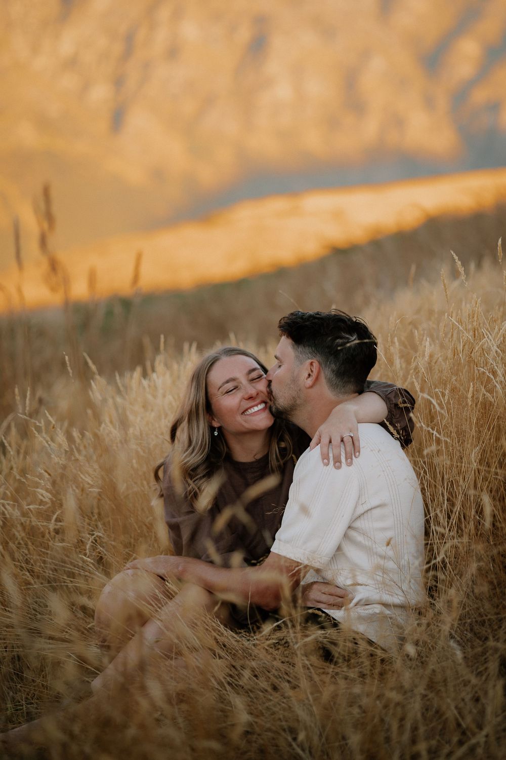 A romantic couple shares an intimate moment lying together in a golden wheat field at sunset.