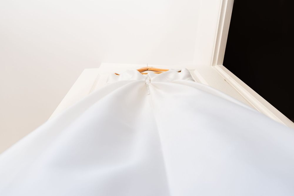 White fabric curtain hanging on a wooden rod against a white wall, with a dark corner visible.