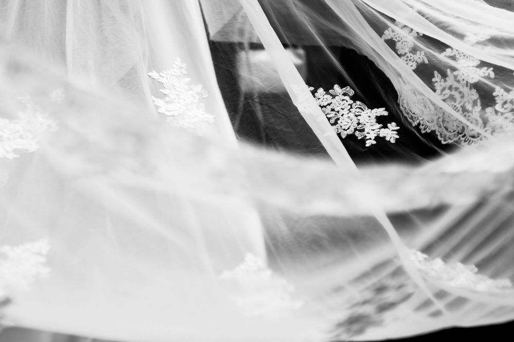 Black and white photo of an elegant lace wedding veil draped softly, showcasing intricate floral embroidery details.