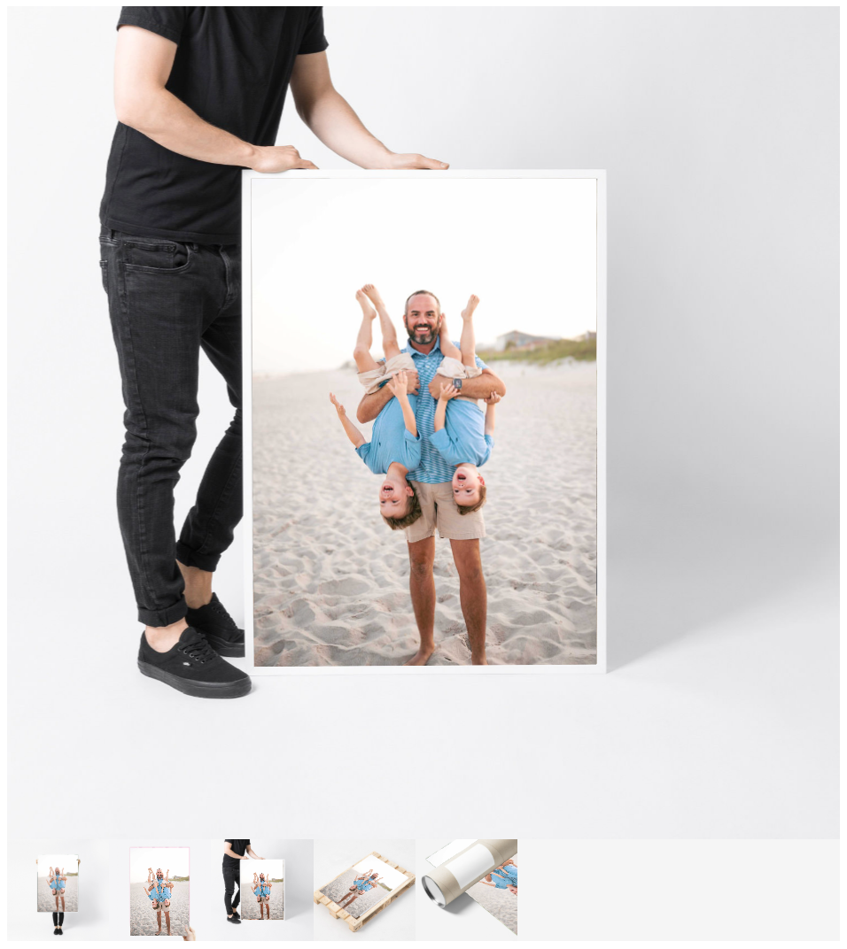 Man holding large framed beach family photo print with children being lifted by father on sandy shore.