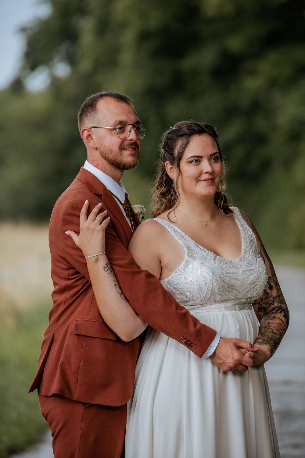 A couple shares a tender moment on their wedding day, with the groom in a rust-colored suit and bride in white.