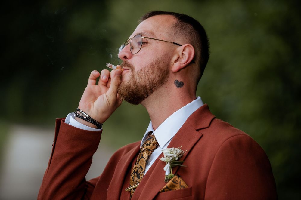 Emotional groom in rust-colored suit and floral tie wipes away tears.