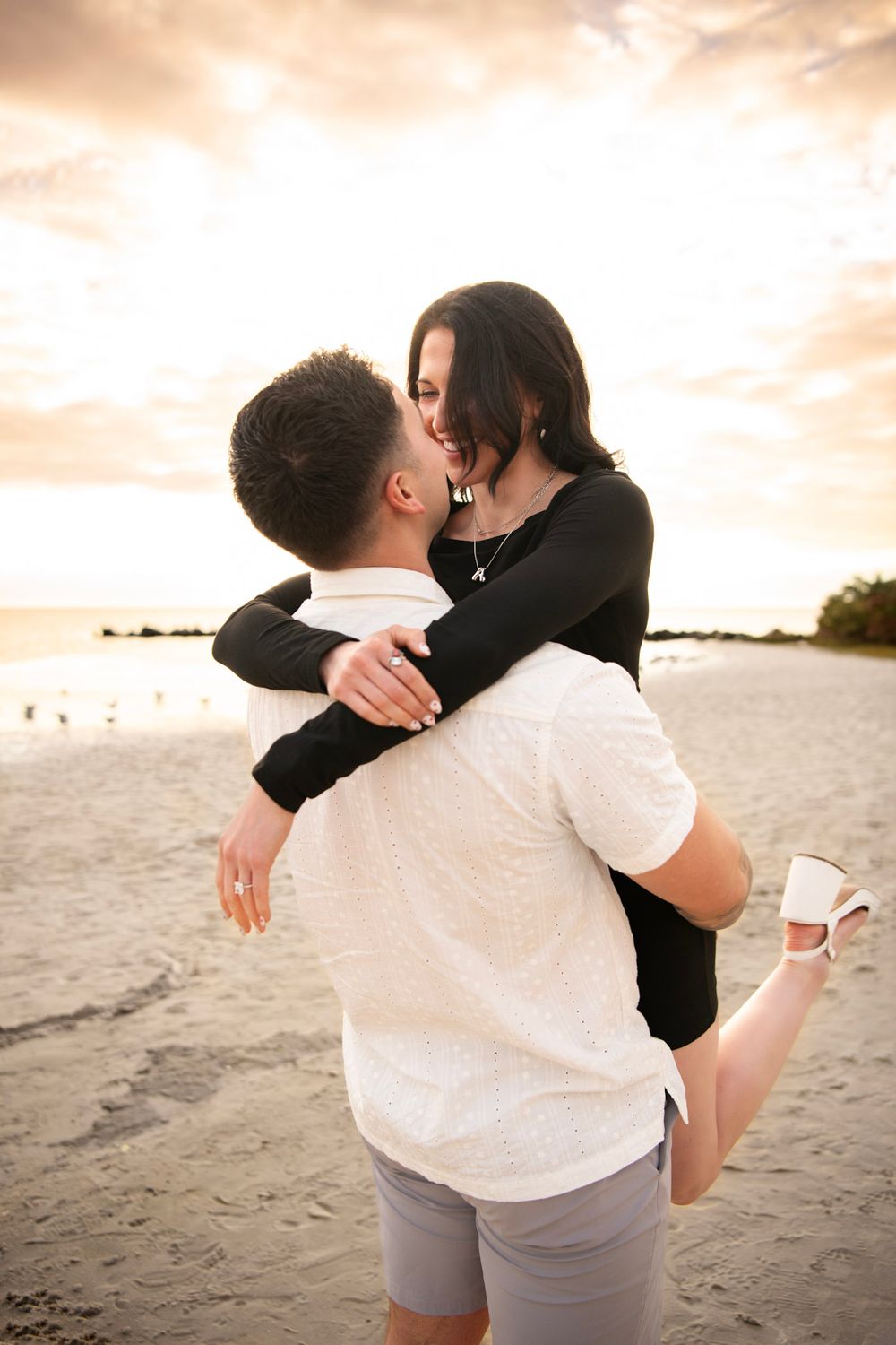 Newly engaged couple embracing on Clearwater Beach after a surprise proposal with soft coastal skies in the background.