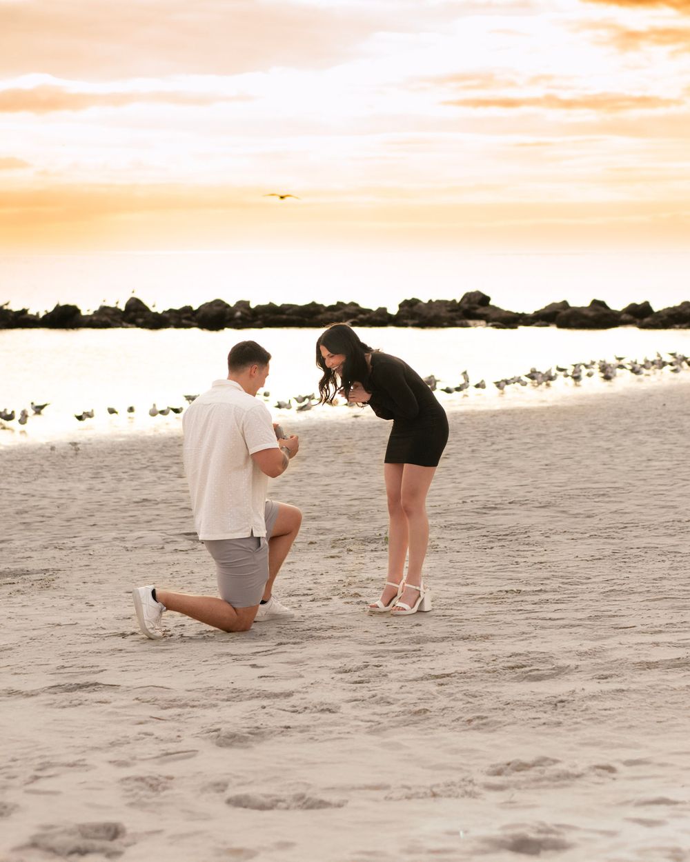 Surprise beach proposal in Clearwater, Florida as a groom-to-be kneels on the sand during a romantic engagement session.