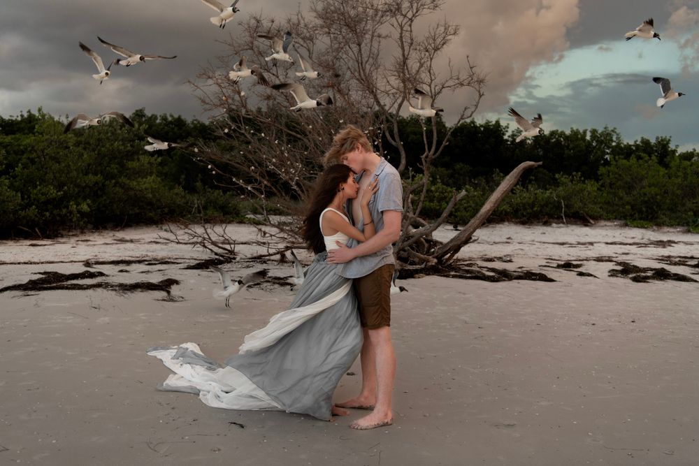 Moody coastal couples portrait at Honeymoon Island featuring rolling waves, sea birds, and summer storm skies.