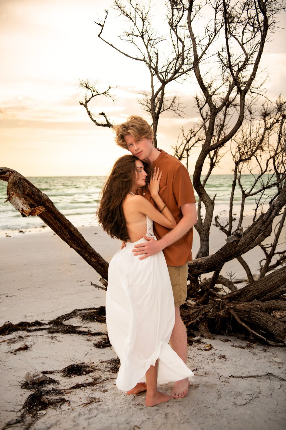 Intimate beach photography session in Dunedin, FL with a couple framed by driftwood and Gulf Coast scenery.