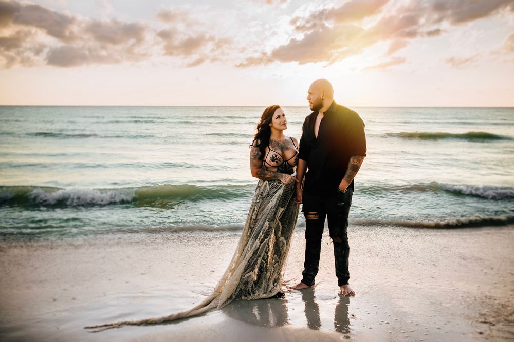 Romantic Dunedin FL couples photos featuring a tattooed couple walking barefoot along the shoreline at sunset.
