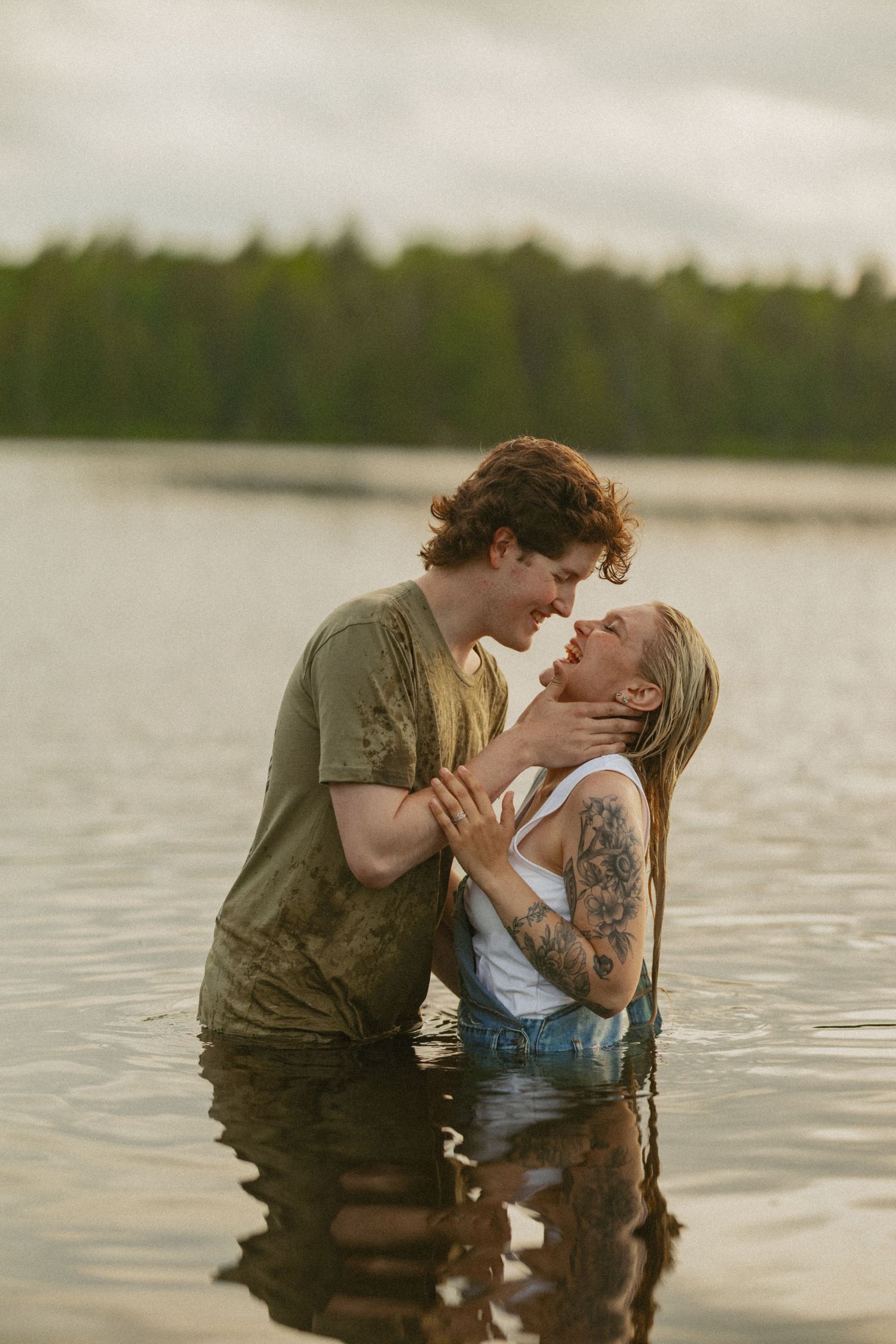 Romantic couple sharing a tender moment while standing waist-deep in a calm lake, surrounded by lush forest.