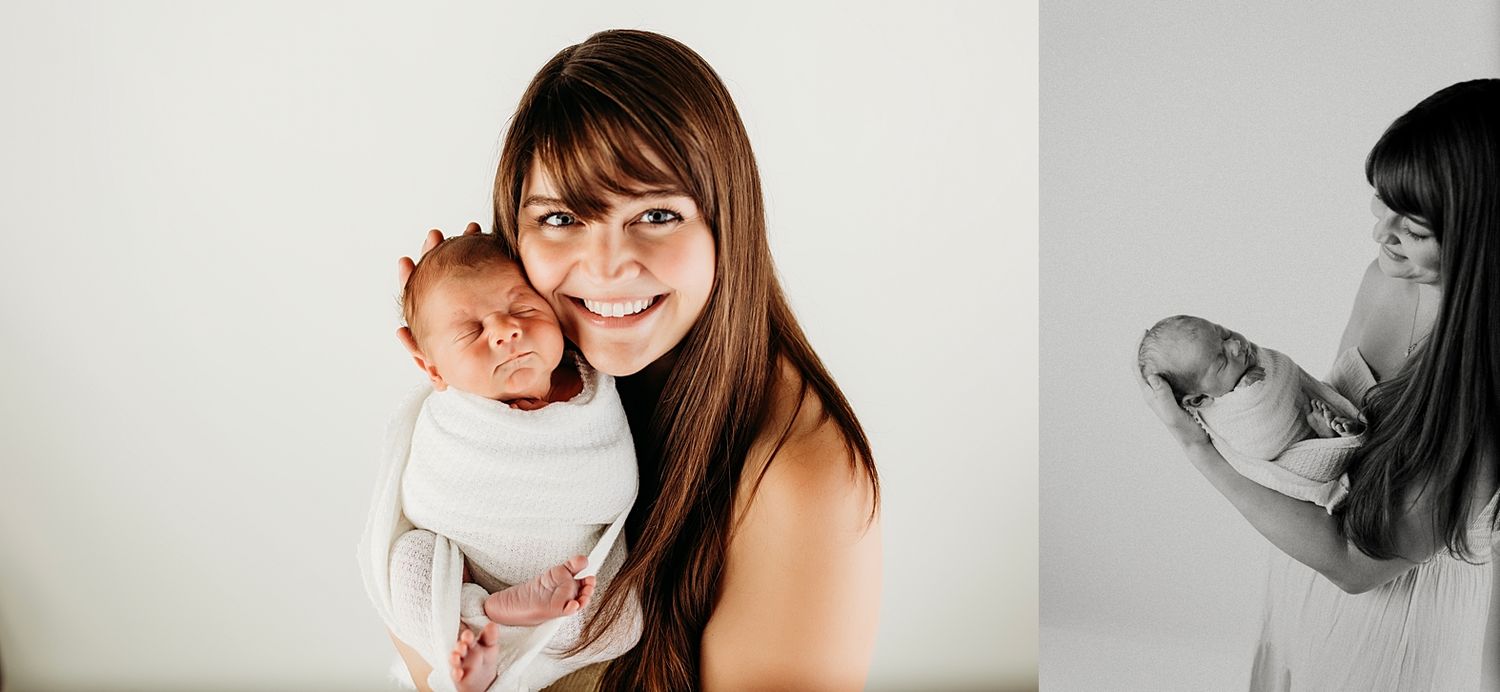 A smiling mother with long brown hair holds her swaddled newborn baby in a bright studio portrait.
