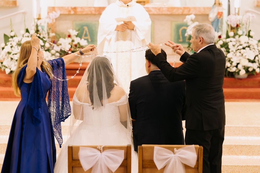 Catholic wedding ceremony in church with bride and groom kneeling at altar while officiant performs traditional rites.