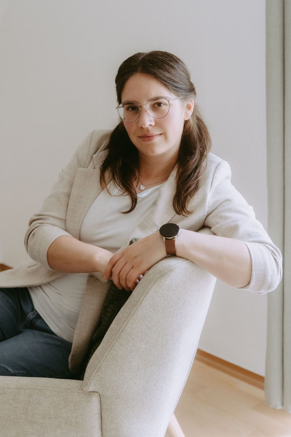 Young woman with glasses and watch relaxing on a gray sofa in a bright modern room.