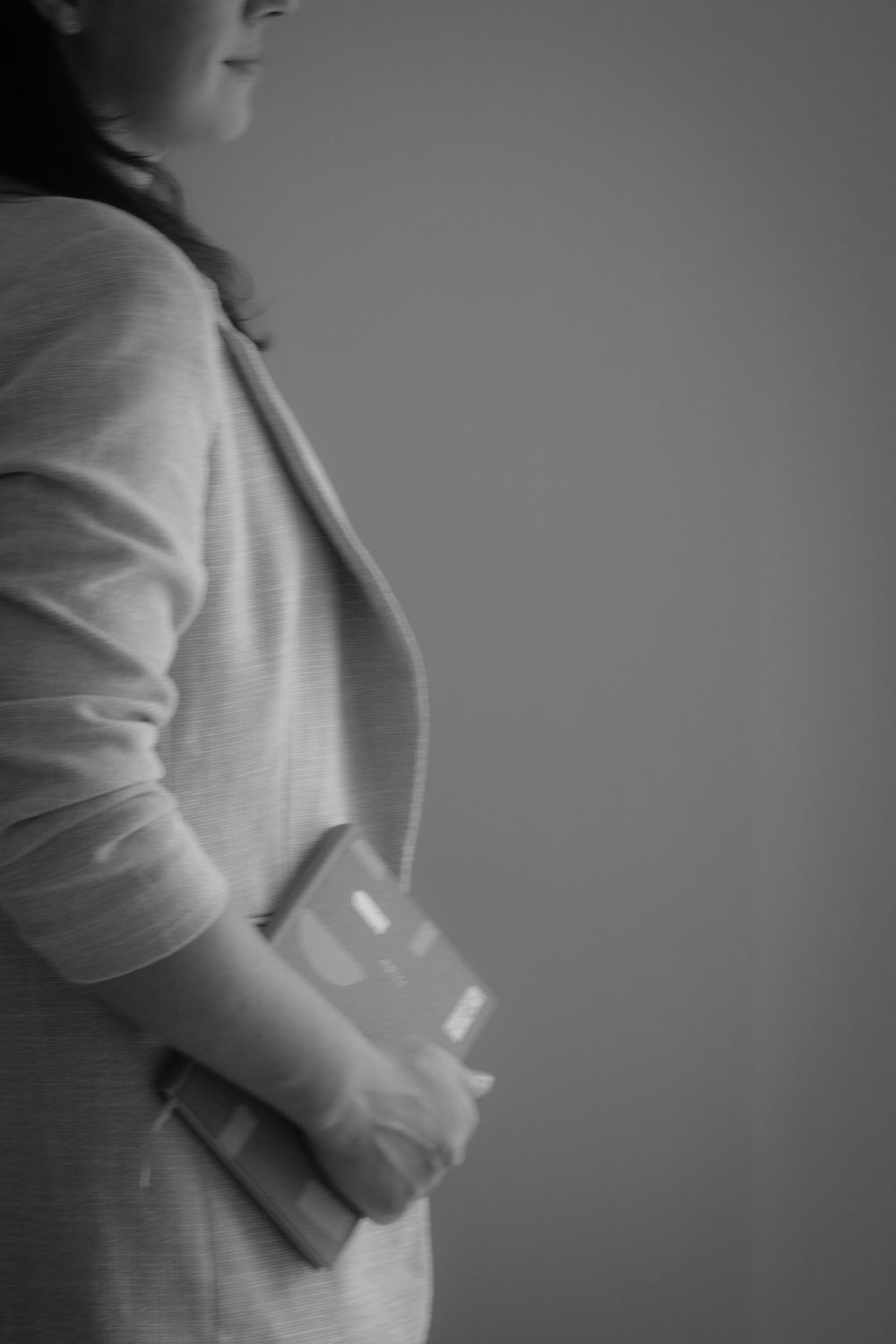 Black and white photo of a pregnant woman in a cardigan holding a book against her baby bump.