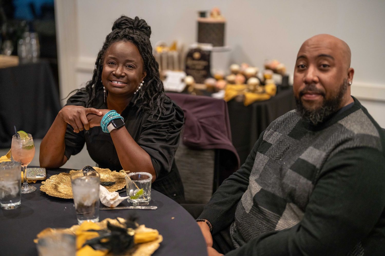 Two people smiling at a banquet table with food and drinks at a formal event.