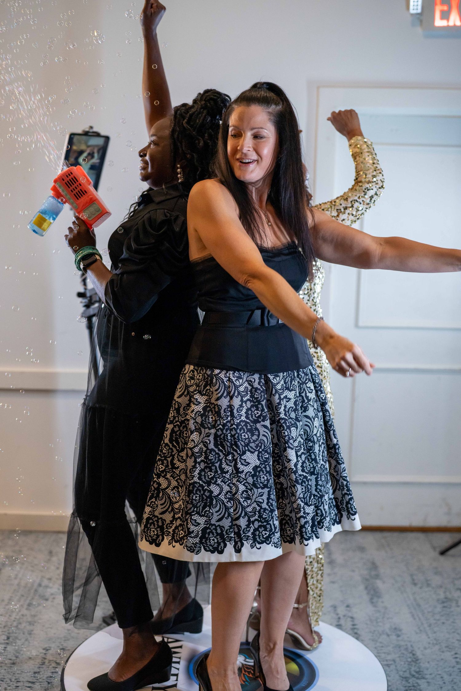 Two women dancing joyfully at a party, one in a black lace dress, celebrating with raised arms and big smiles.