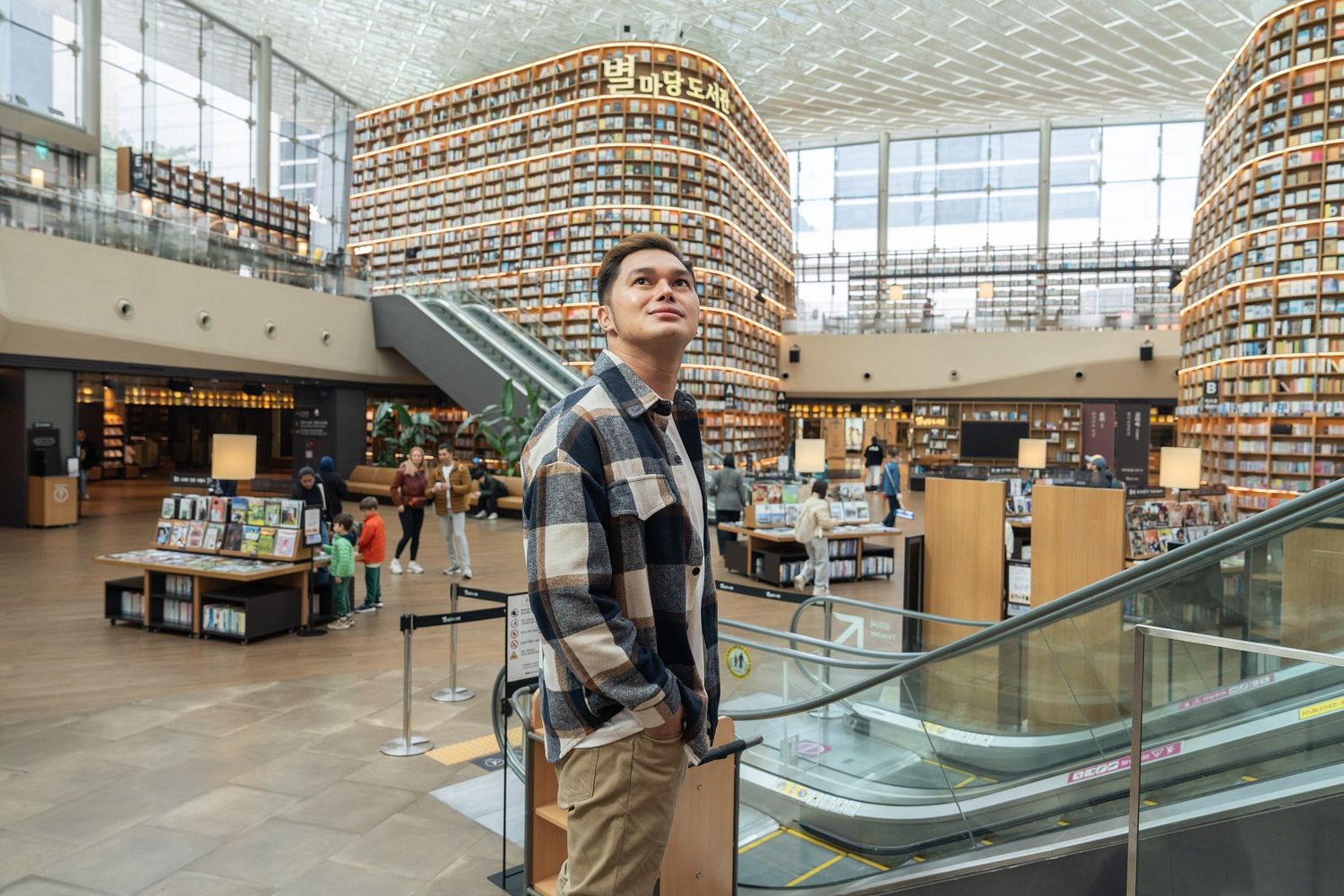 Man standing in a modern library atrium surrounded by towering bookshelves filled with books.