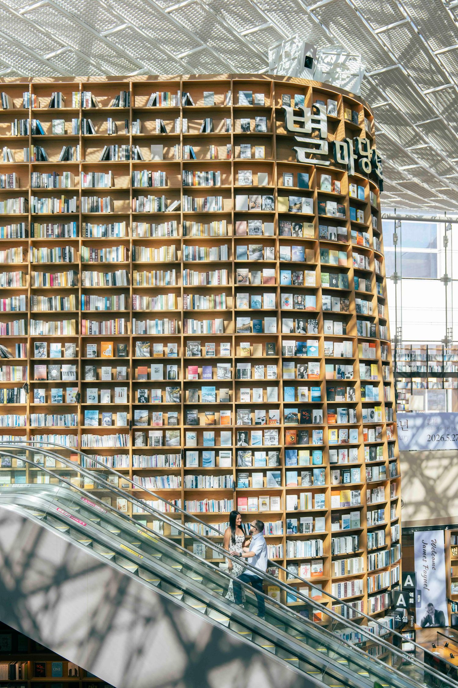 Towering curved bookshelves fill the Starfield Library in COEX Mall, Seoul, with visitors on an escalator below.