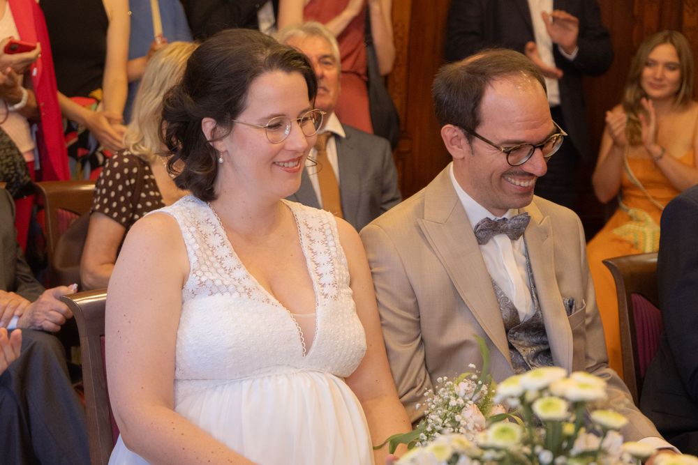 Smiling bride in white dress and groom in suit sitting together during their wedding ceremony indoors.
