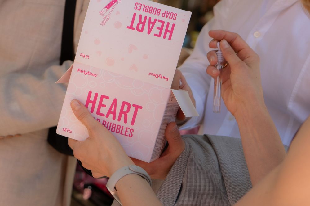 Hands holding pink Heart Soap Bubbles packaging boxes at a wedding or event celebration.