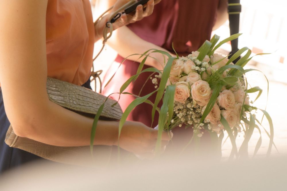 Close-up of a bride holding a delicate bouquet of white and pink roses with greenery at a wedding ceremony.