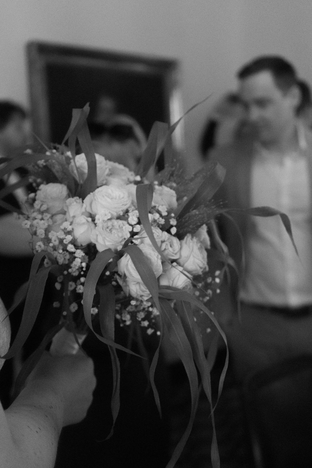 Black and white photo of a bride holding a wedding bouquet with roses and baby's breath at a wedding ceremony.