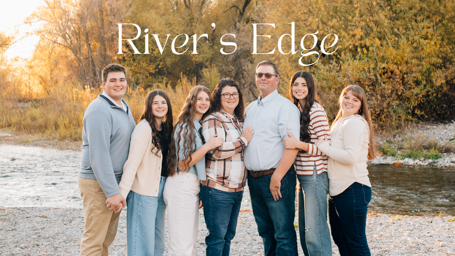 Family of seven posing outdoors near a river in autumn, with text overlay reading Rivers Edge.