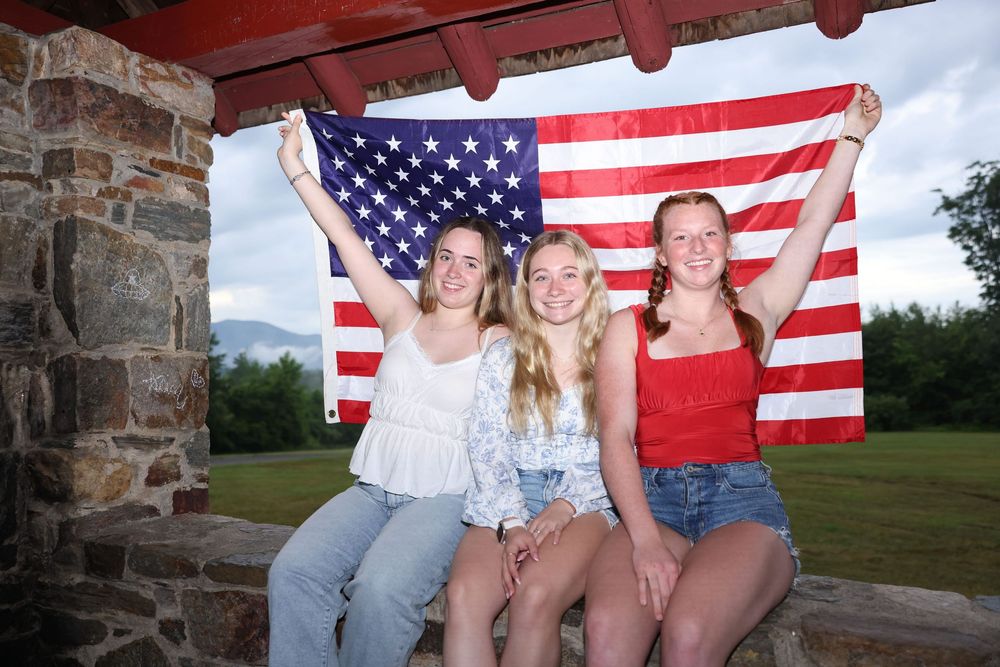 Three young women holding an American flag outdoors, celebrating Independence Day together.