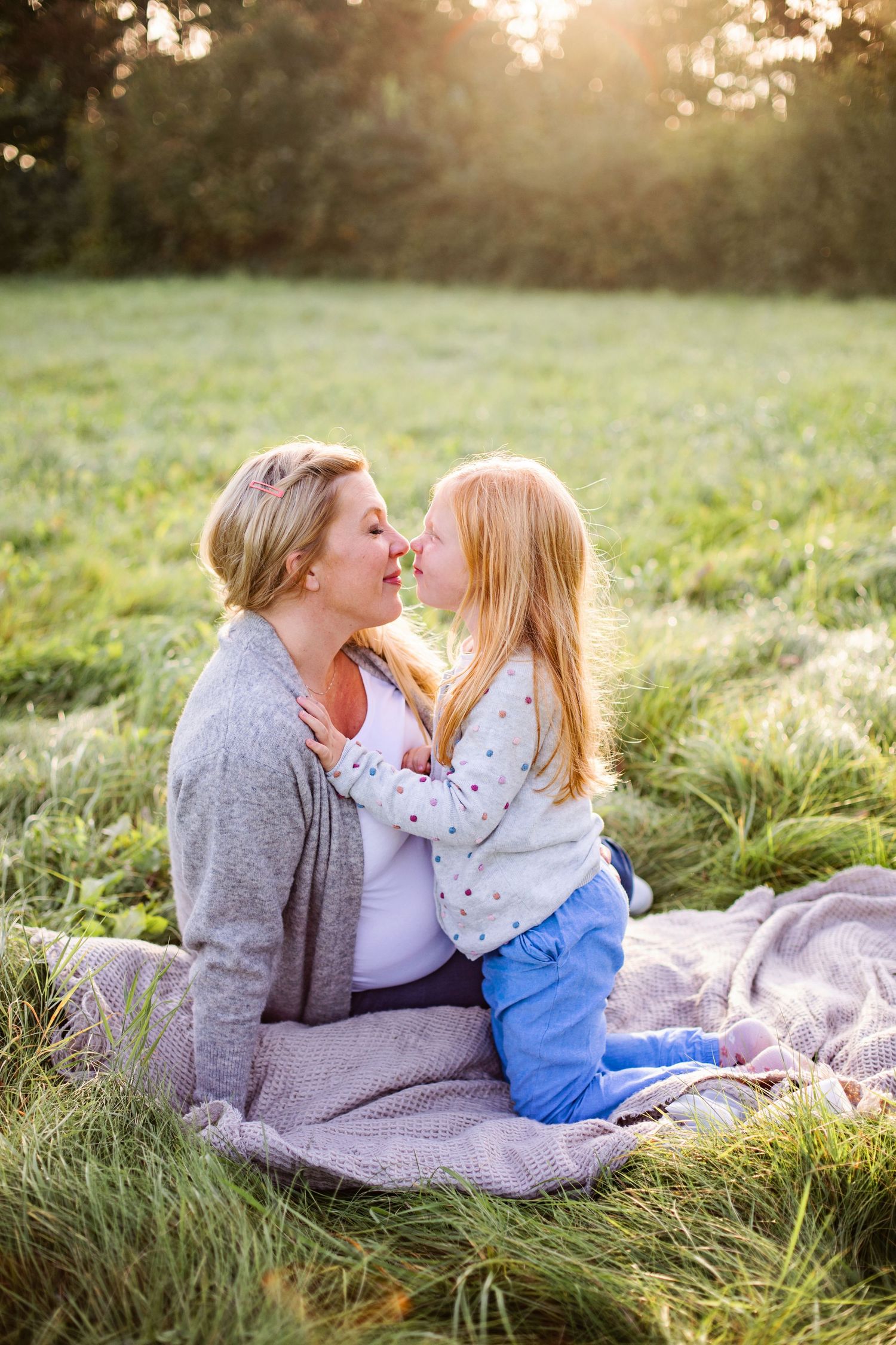 A family in vintage-inspired attire poses together at sunset in a grassy field during golden hour.