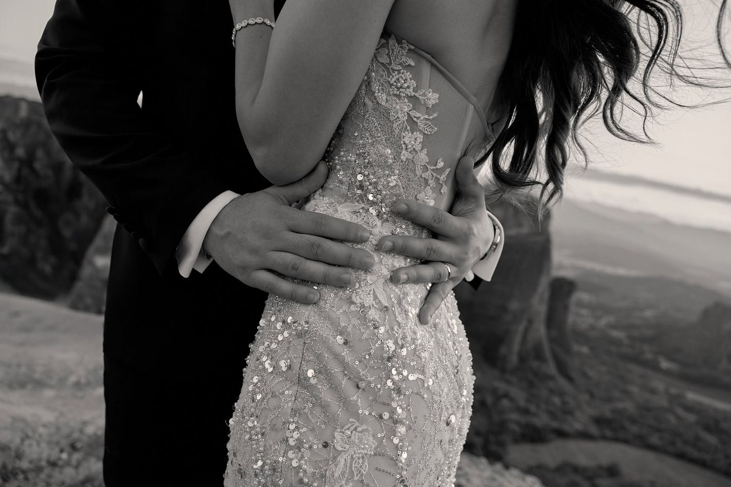 Black and white close-up shot of the groom embracing his bride around her waist.