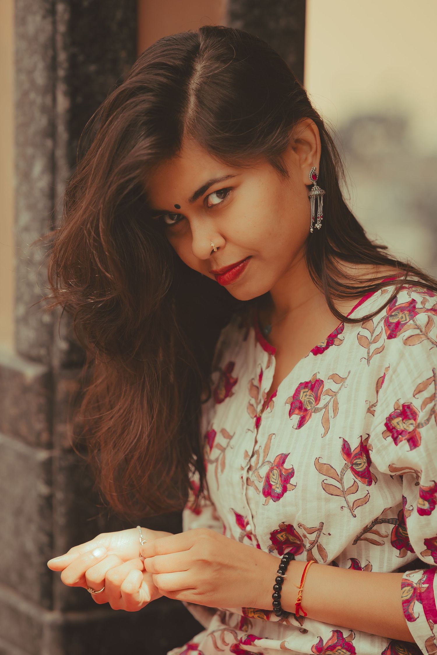 Young Indian woman in floral kurta with red lips and earrings looking sideways outdoors.