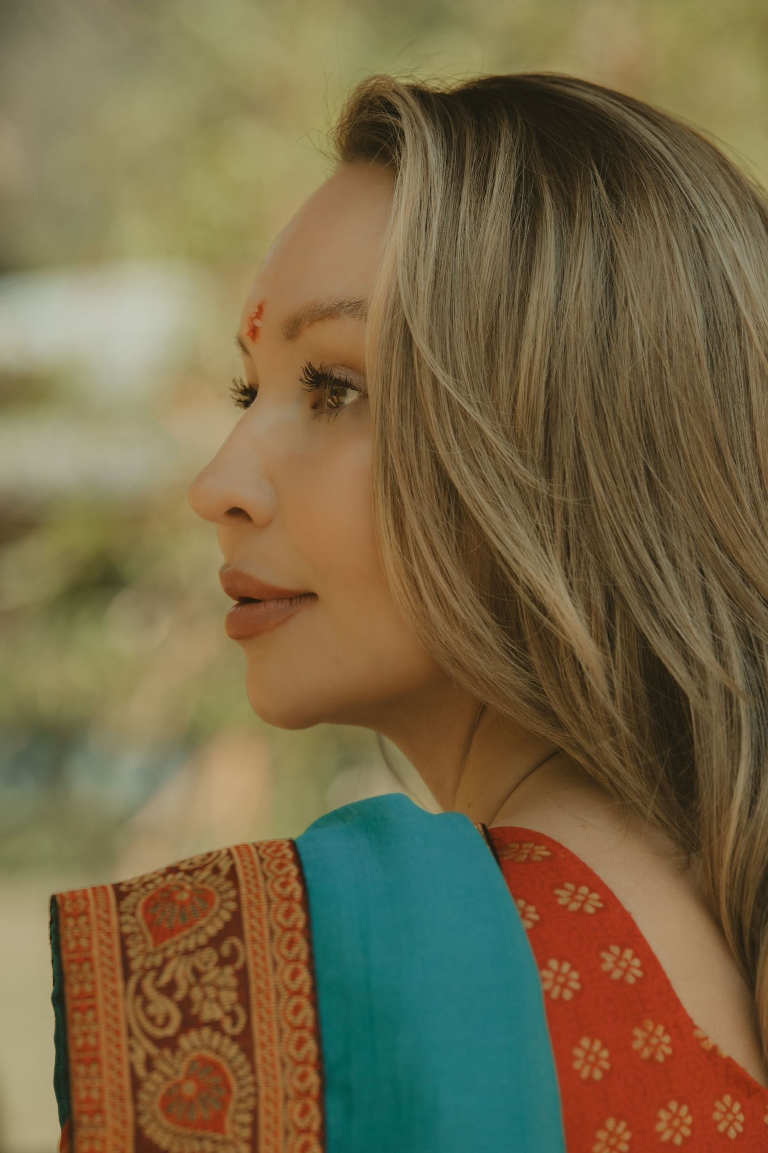 Side profile of woman with blonde highlights wearing traditional Indian sari and red bindi.