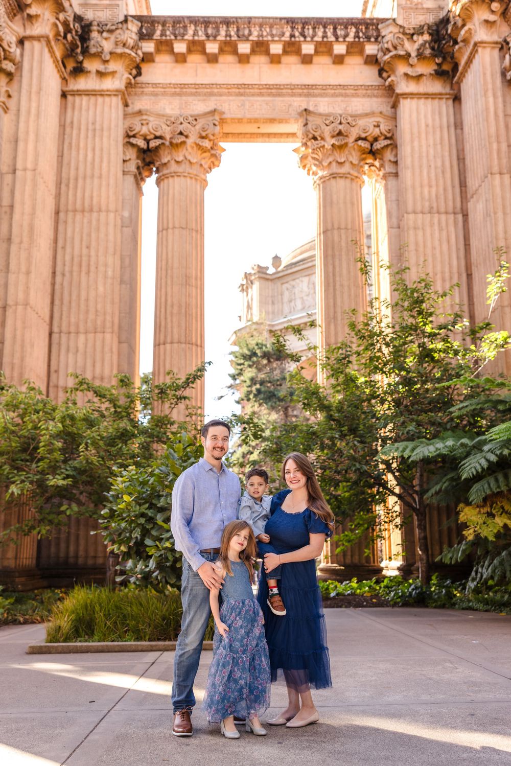Family of four posing together at the Palace of Fine Arts in San Francisco, surrounded by grand columns and lush greenery.