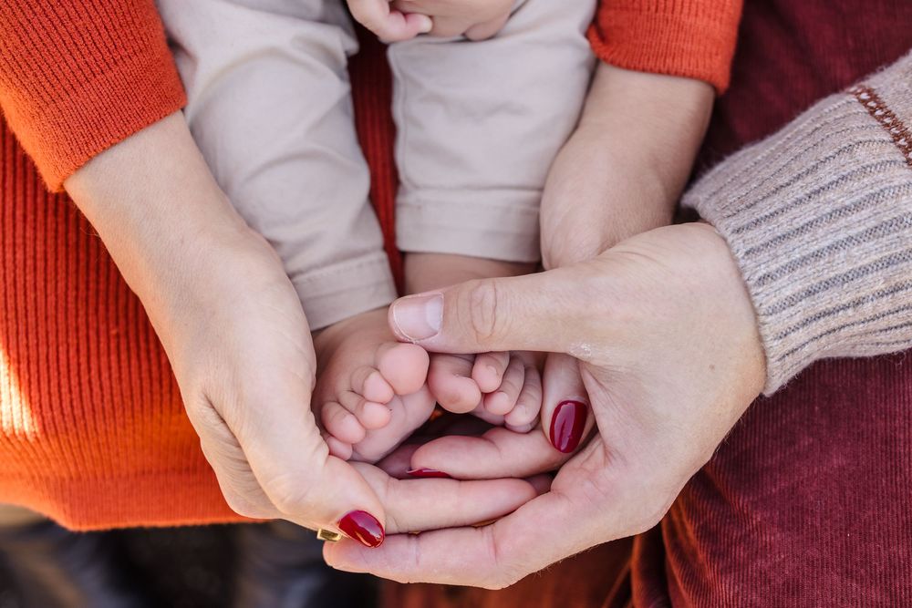 Two adults cradle a baby's tiny feet in their hands, symbolizing family love and new parenthood.