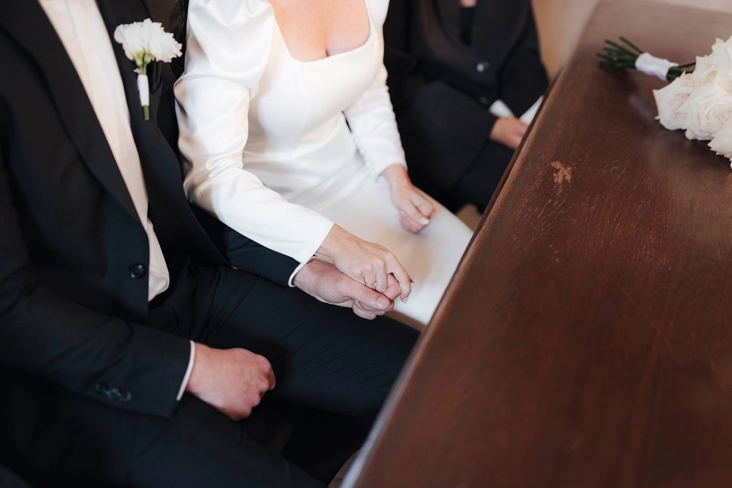 Emotional bride and groom wiping tears during wedding ceremony at elegant venue with guests in background.