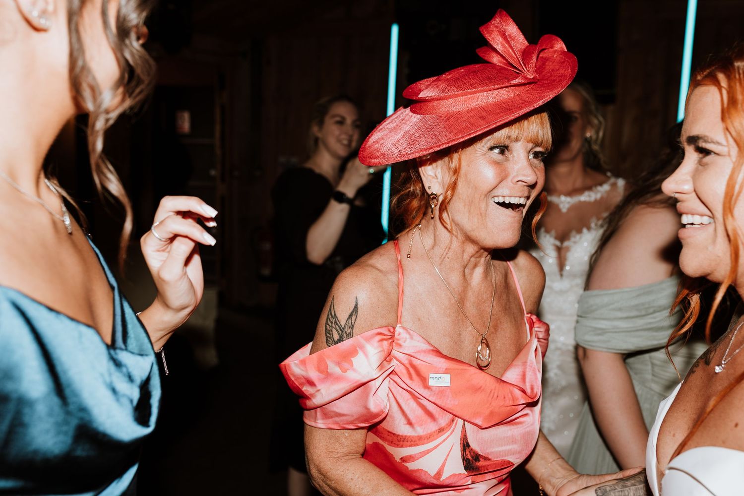 Woman in pink dress and red fascinator hat smiling and dancing at a wedding reception party.