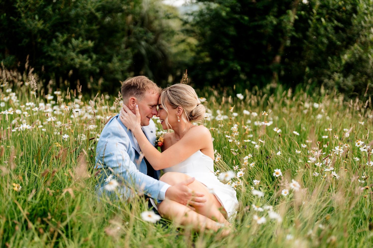 Couple sharing romantic kisses in a field of wildflowers and tall grass on a sunny summer day.