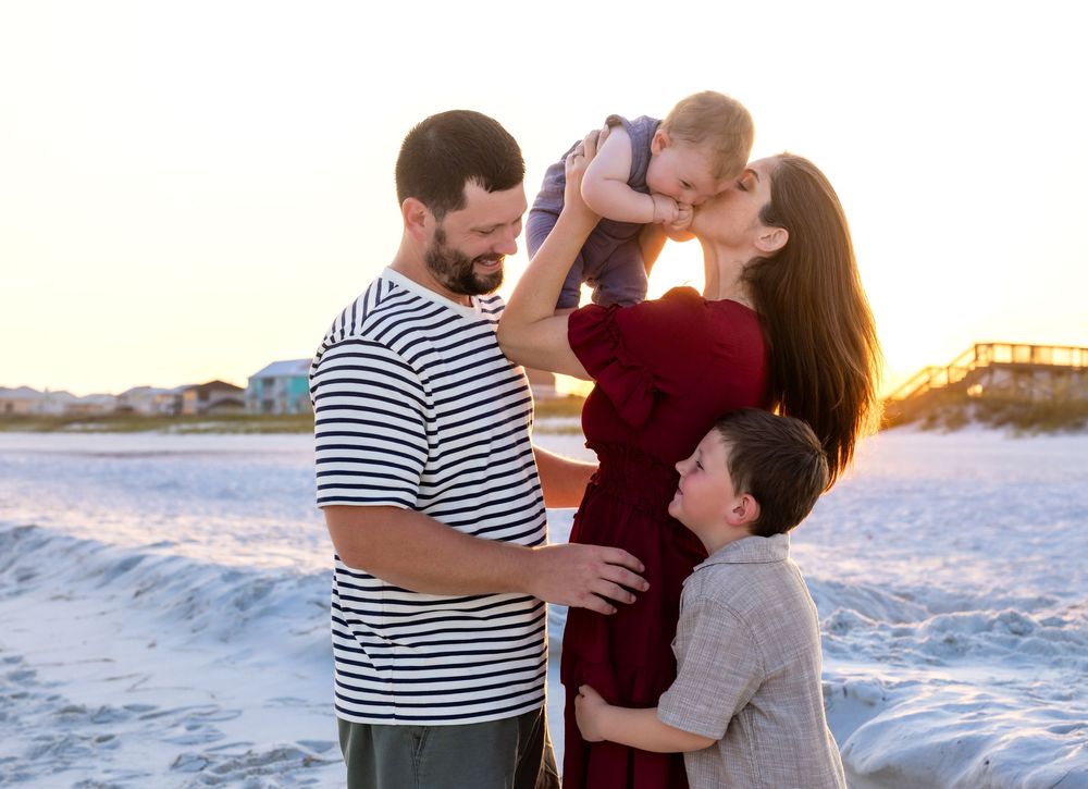 Family of four enjoying a golden sunset beach session, parents holding children close on sandy shore.