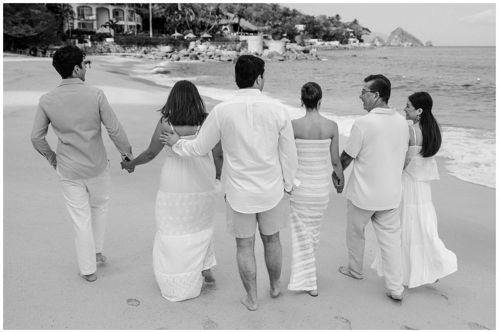 Puerto Vallarta Family Photographer captures Family Photo Session moments of a group walking hand in hand along a sandy beach by the ocean.