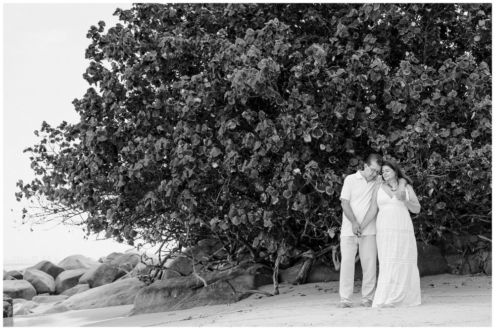 Puerto Vallarta Family Photographer captures Beach Photoshoot moments of a couple standing beneath a large tree on a quiet sandy beach.