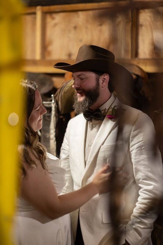 Bearded groom in cowboy hat and white suit shares first dance with bride in rustic barn wedding venue.