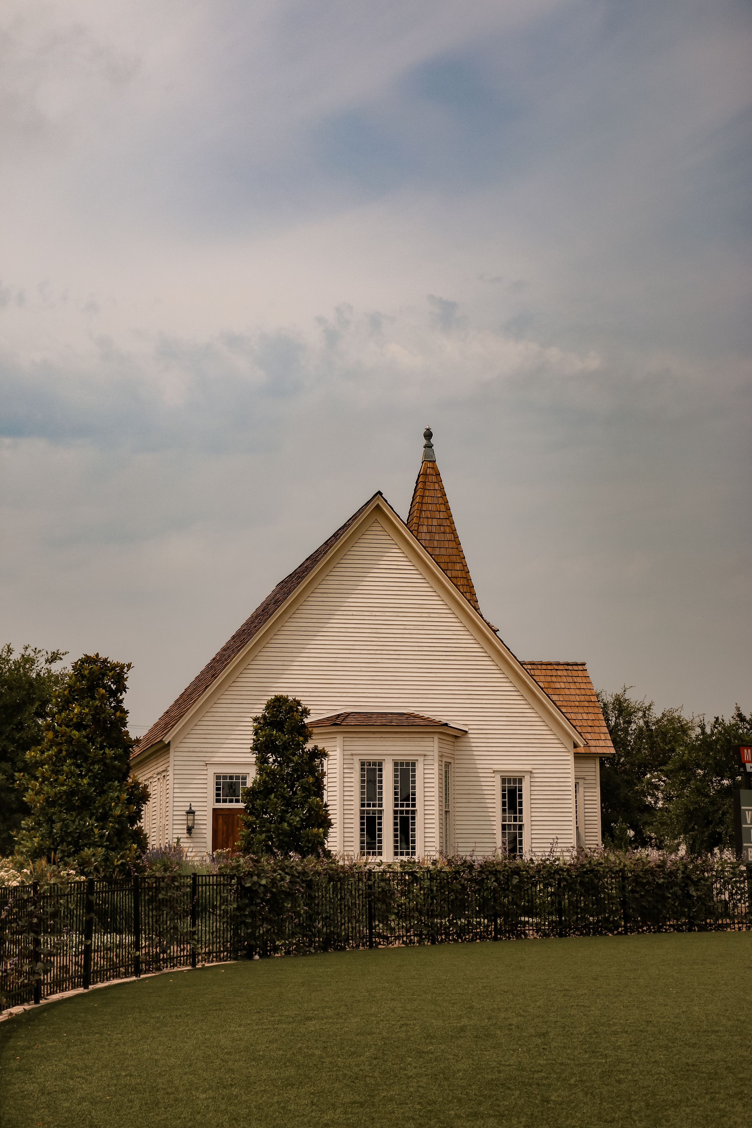 White Gothic Revival church with pointed spire against cloudy sky.