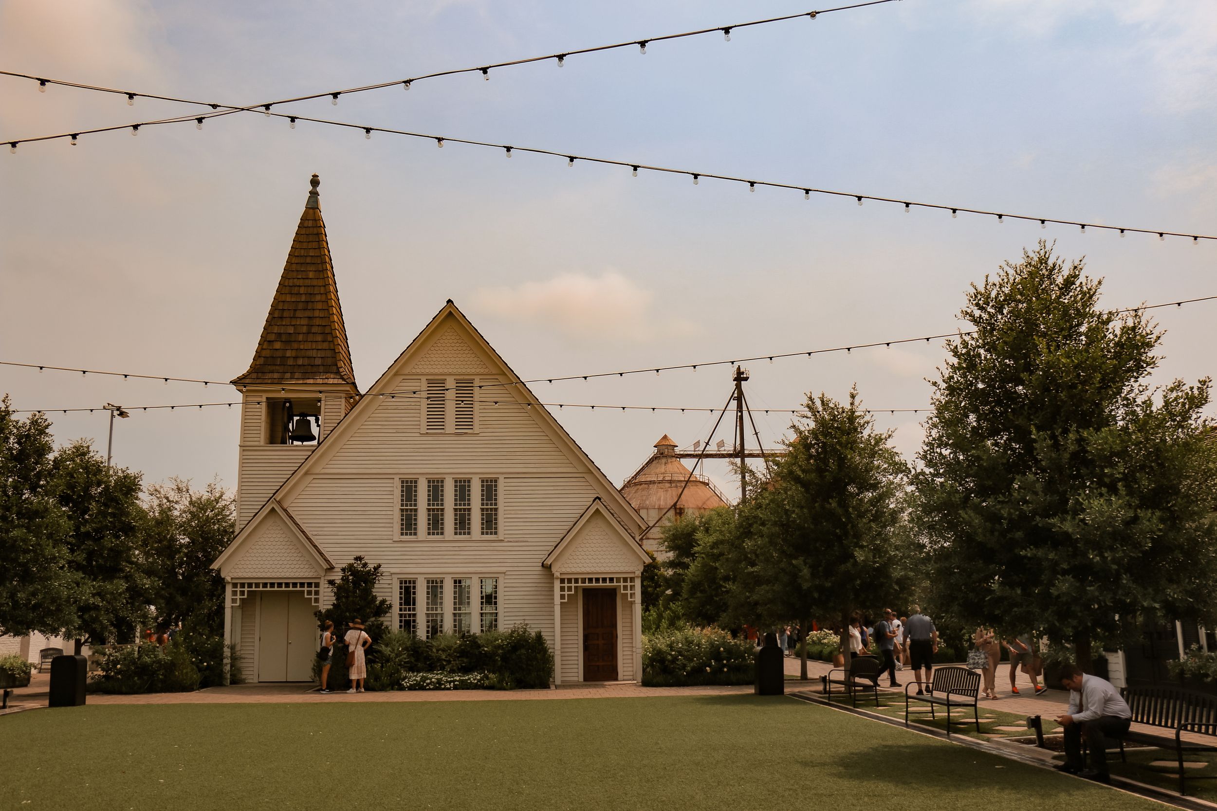 White church building with string lights and spire under evening sky.
