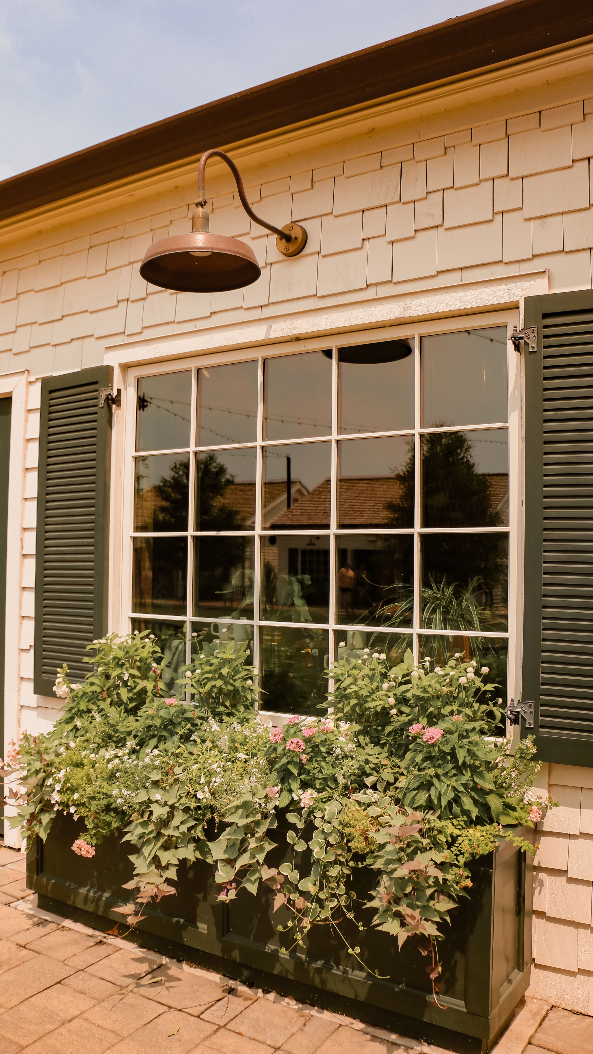 Window with green shutters and flower box mounted beneath copper gooseneck lamp.