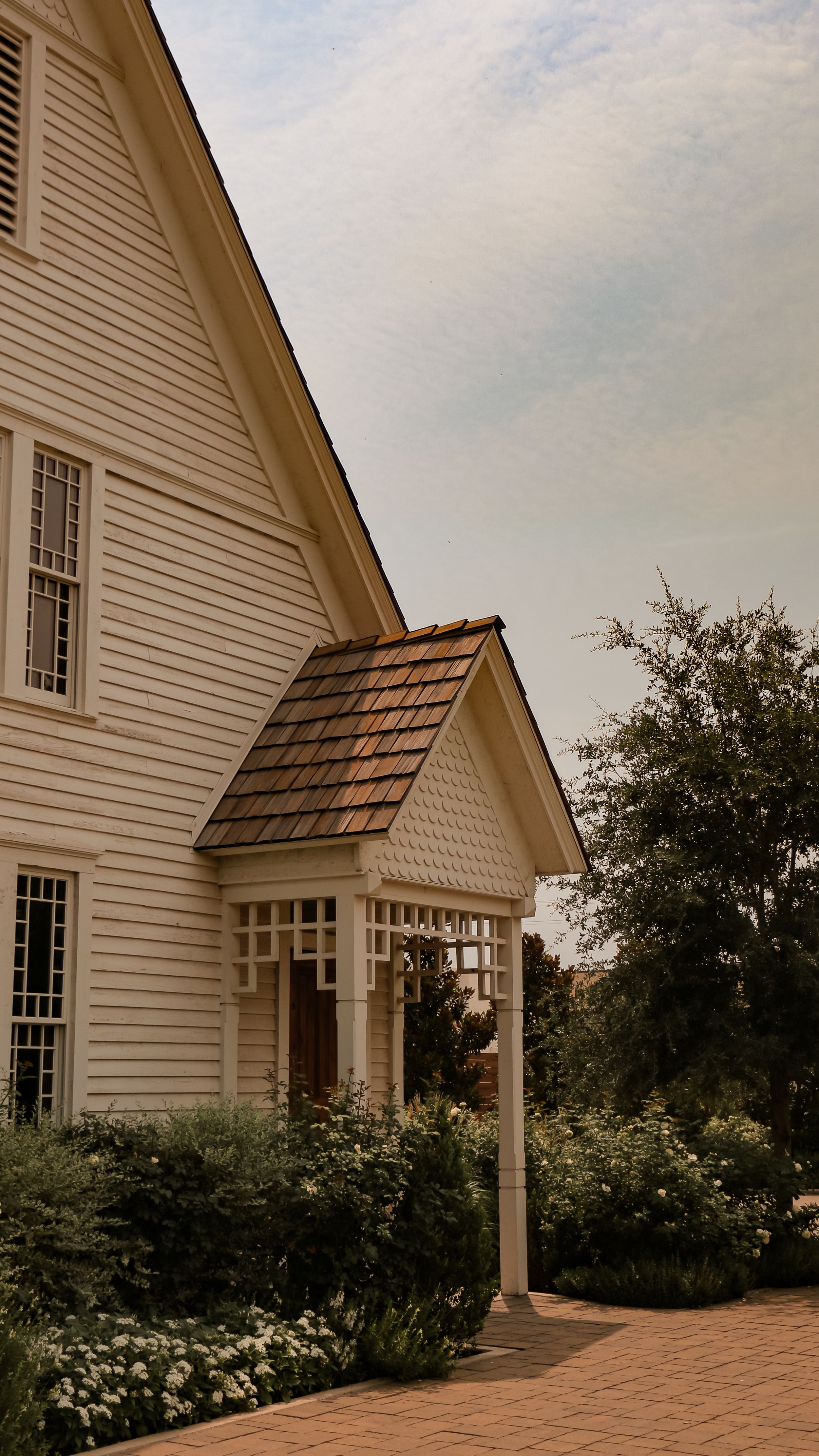 White clapboard house with shingled entry porch and manicured garden.