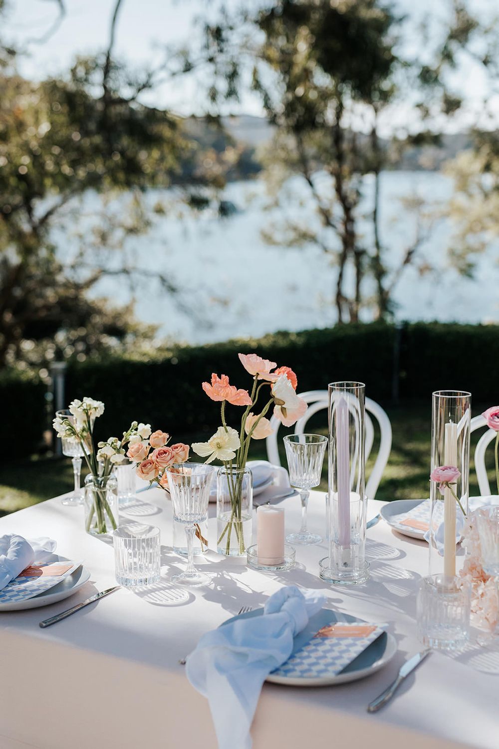 Close-up of elegant wedding table setting with pink flowers, candles, and blue linen napkins.