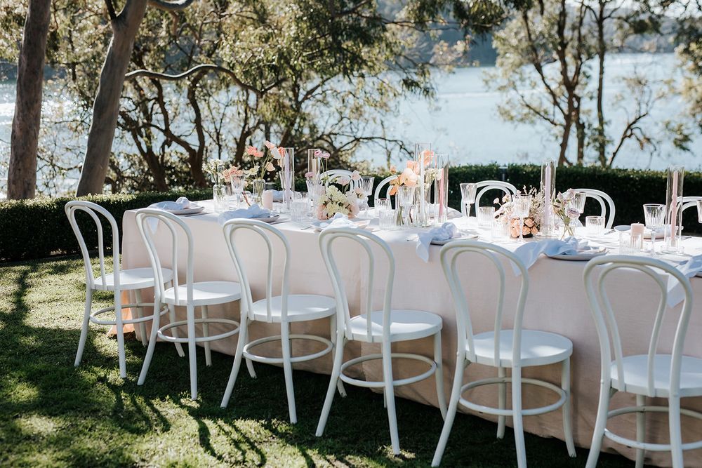 Elegant outdoor wedding reception table with white Thonet chairs, floral centerpieces, and waterfront views.