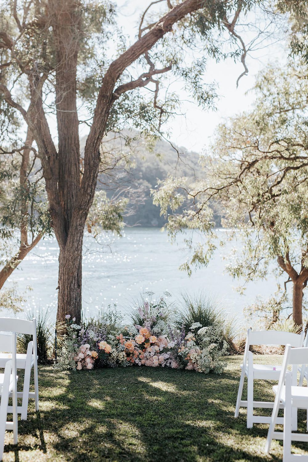 Romantic outdoor wedding ceremony setup with floral arrangement beside trees overlooking a serene lake.